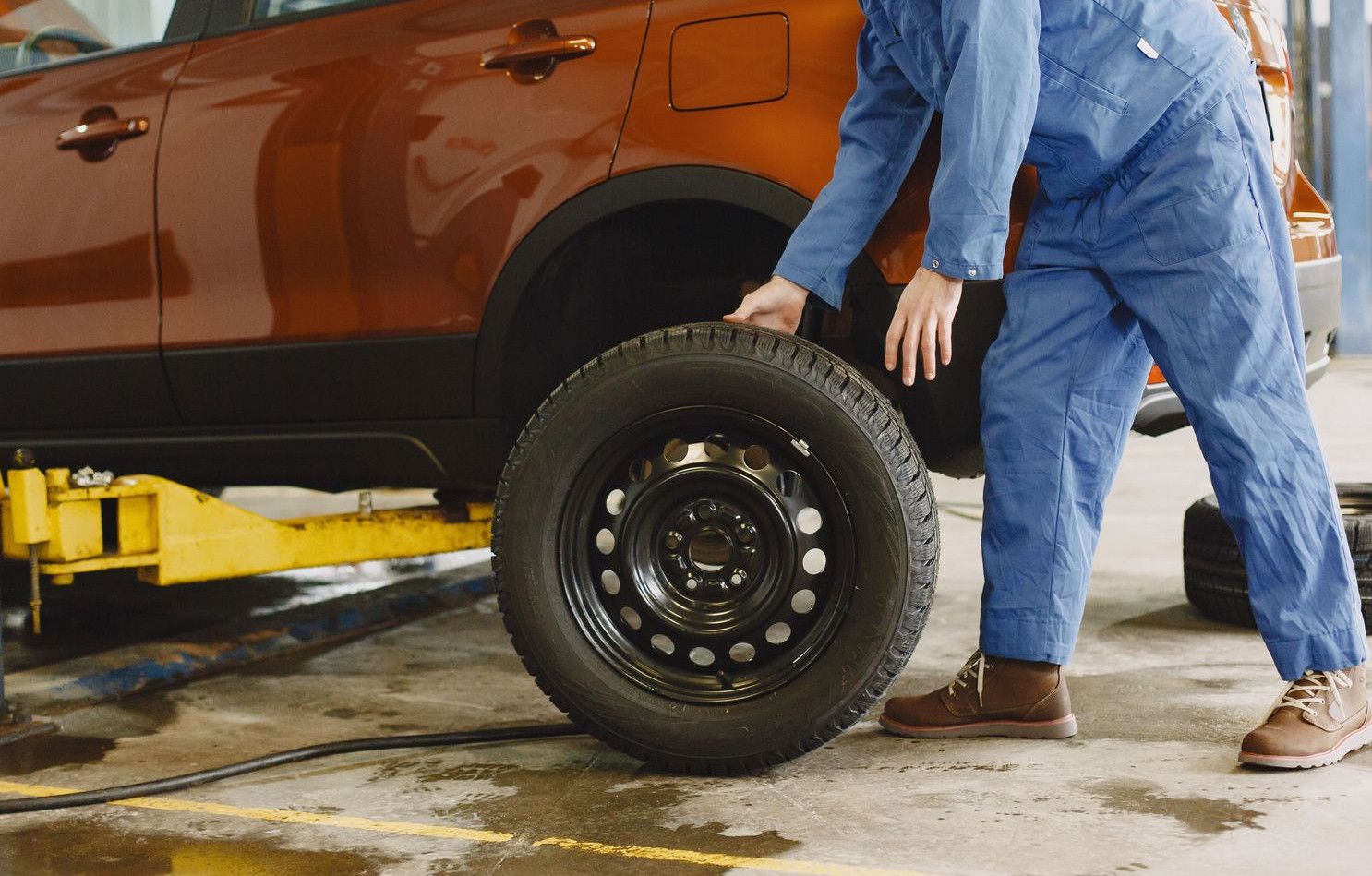 Mechanic in blue coveralls replacing tire on red SUV in repair shop garage.